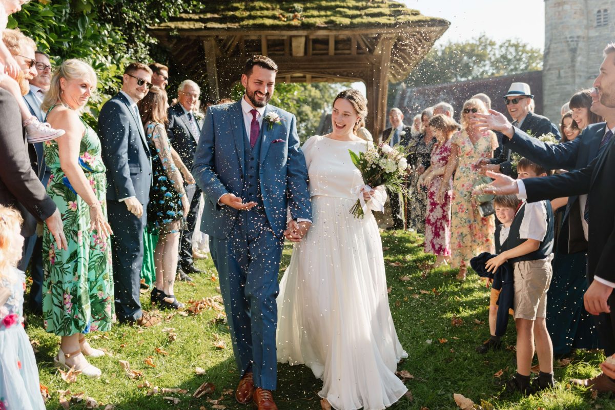 picture of bride and groom leaving service through confetti tunnel